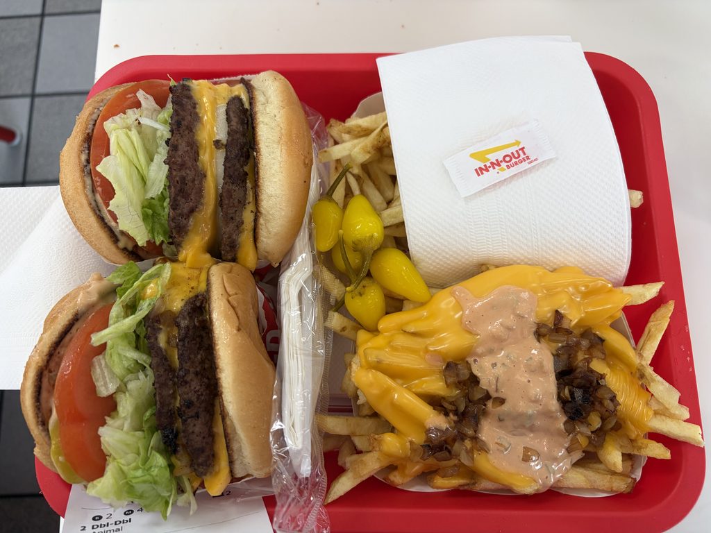In-N-Outの赤いトレイに載ったハンバーガー2個とフライドポテト。右のポテトはチーズソースとスプレッド、刻んだ玉ねぎがかかったアニマルスタイル