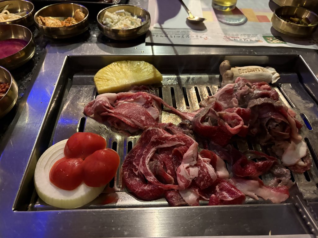 韓国式焼肉店の鉄板グリルに並べられた生のカルビ肉、玉ねぎ、トマト、パイナップル