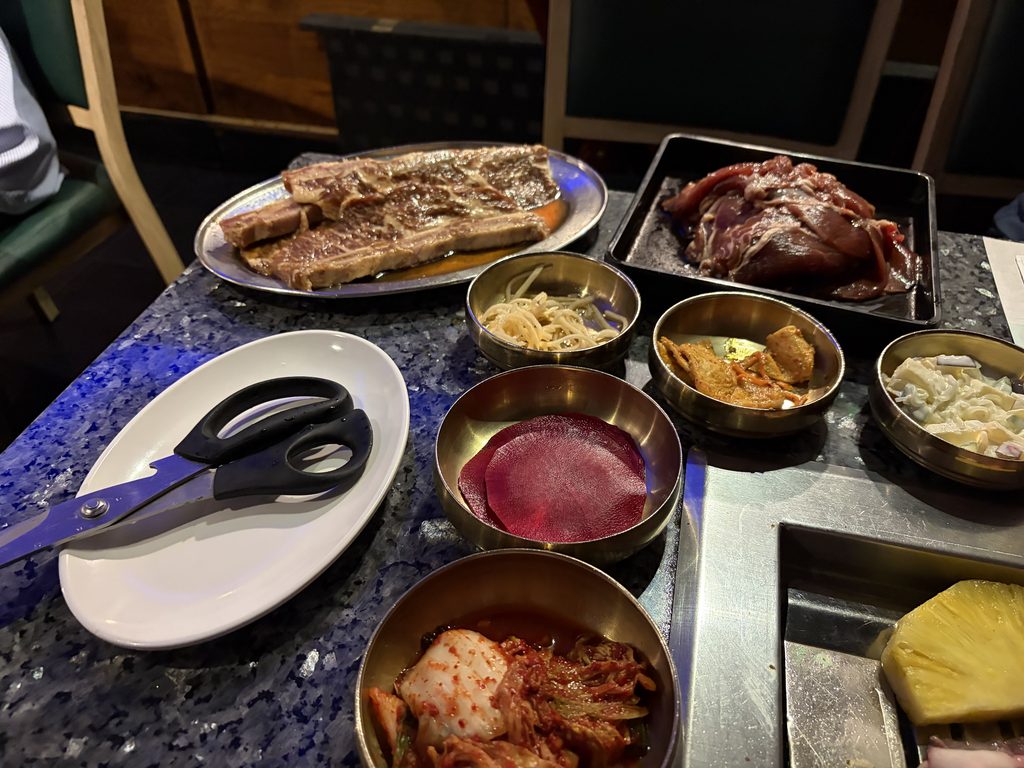 焼き上がったLAカルビと、キムチやナムルなど韓国式の小皿のおかずが並ぶテーブル。手前にキッチンばさみ